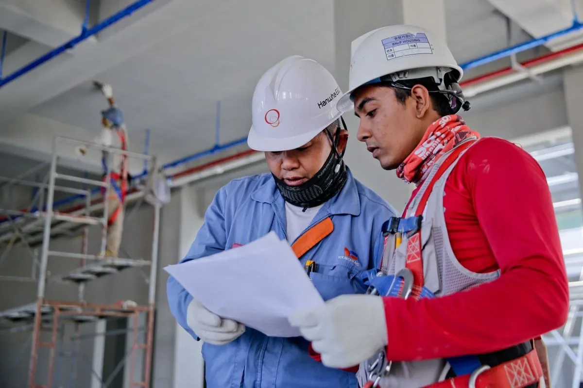 Illustrative stock photo: two engineers in hard hats reviewing plans at a worksite